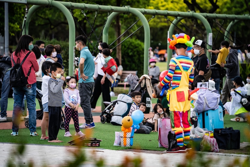 A group of children at a park watch someone dressed in a clown costume.