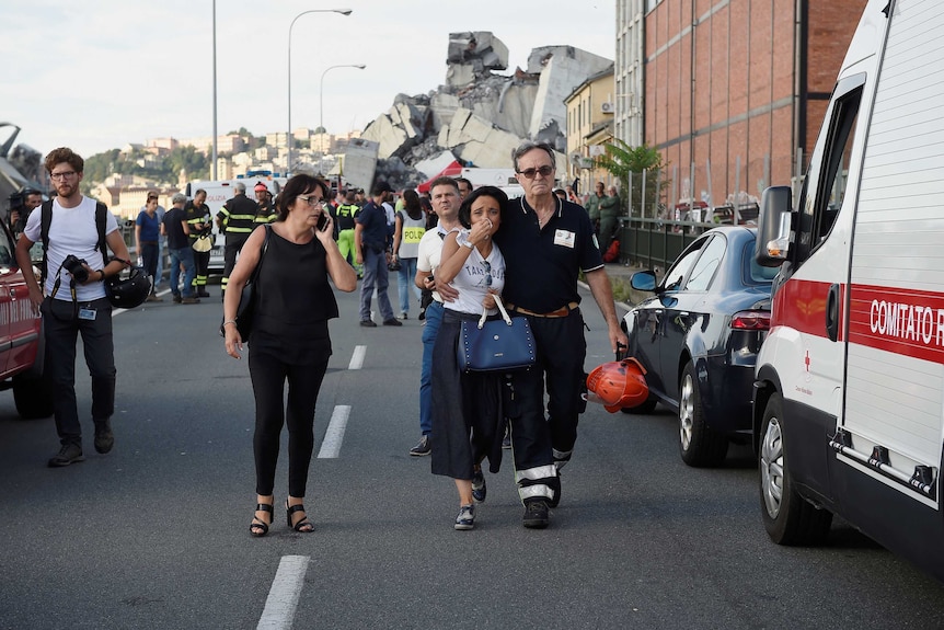 A woman cries being embraced by a fire fighter as she leaves the site of the collapsed Morandi Bridge.