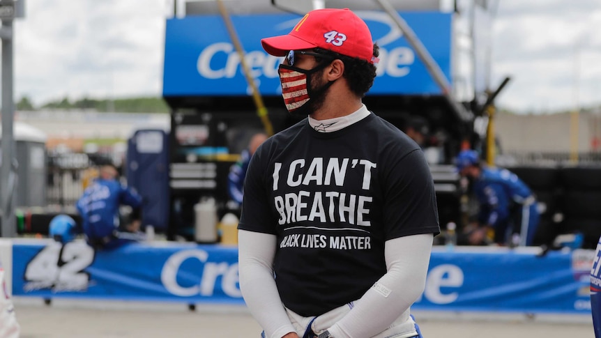 A NASCAR driver stands at a track in a shirt saying "I can't breathe, Black Lives Matter".