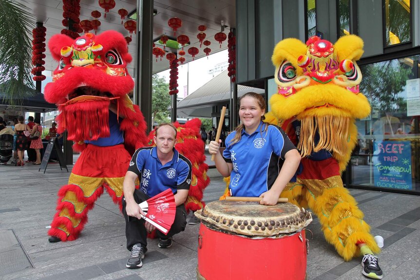 A man with a fan and a girl with a large Chinese drum in front of lion dancers