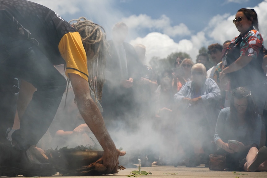 A man leaning down to pick up a bowl of smoking leaves in a crowd