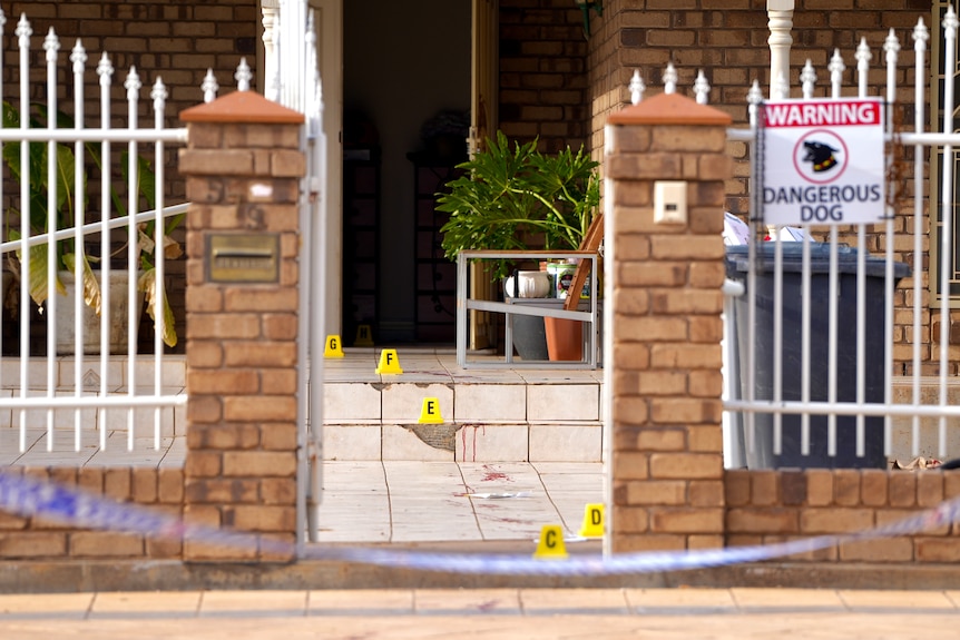 Police tape and bloodied steps at a home with a gate in it