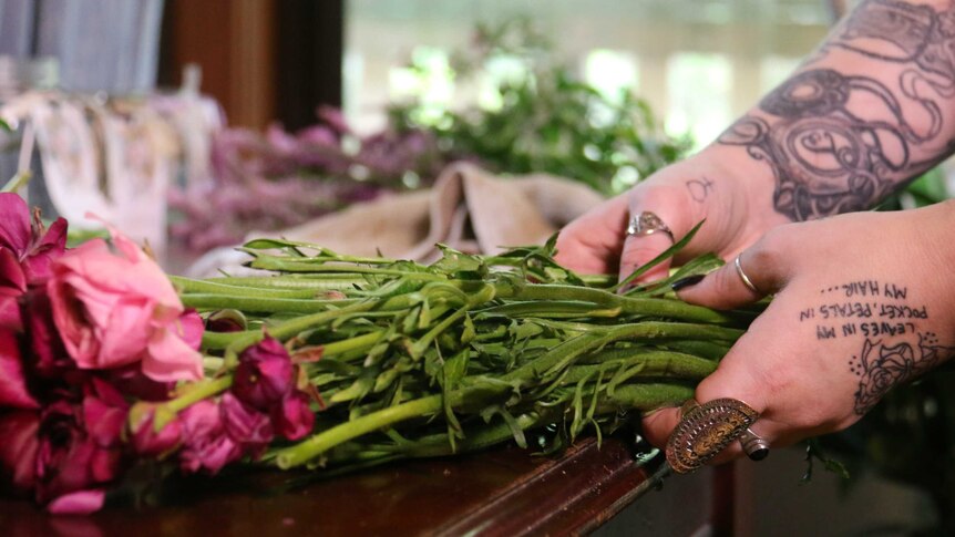 A woman's hands working on a flower arrangement.
