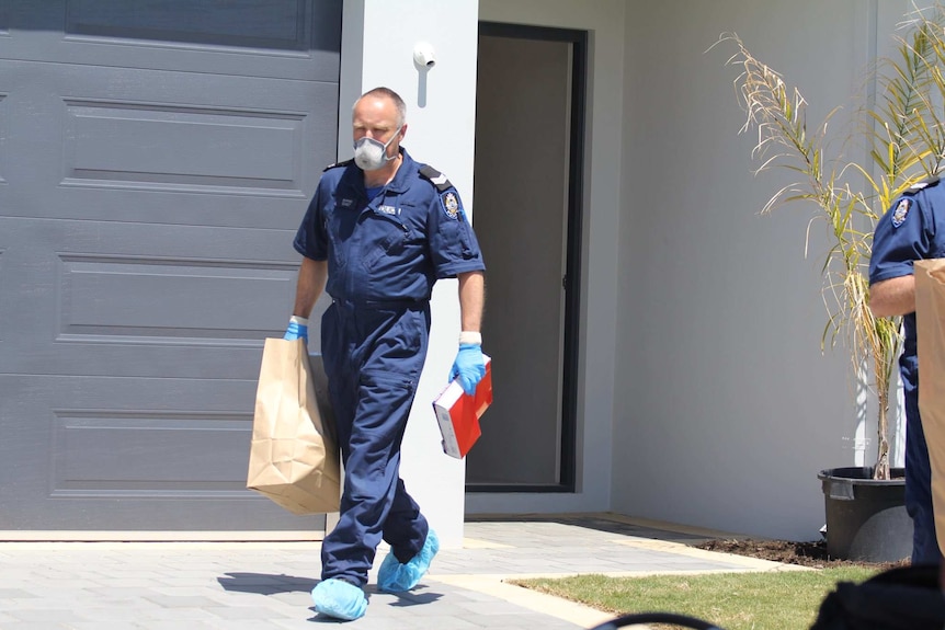 A forensics officer carrying a bag and other items walks out of a house.