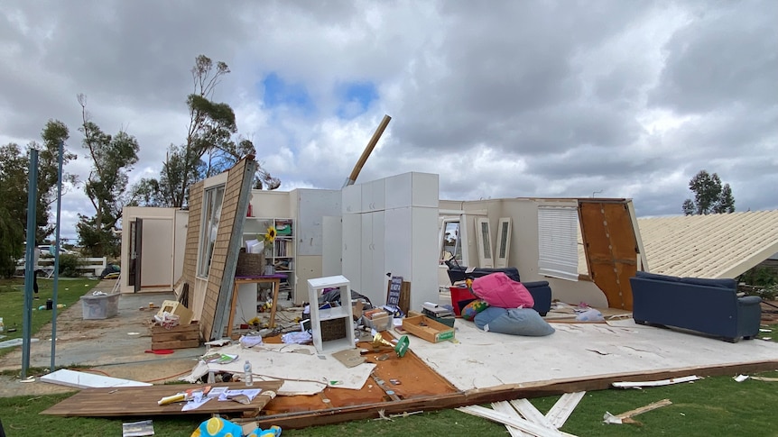 A photo of a home taken from the side with no roof and its walls leaning. All rooms and furniture are exposed.