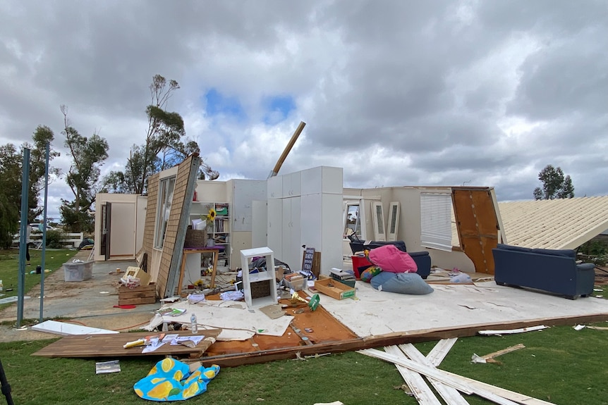 A photo of a home taken from the side with no roof and its walls leaning. All rooms and furniture are exposed.