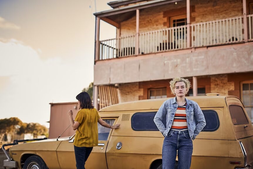 Julia Garner stands infront of an old mustard car parked at the front of the pub The Royal Hotel