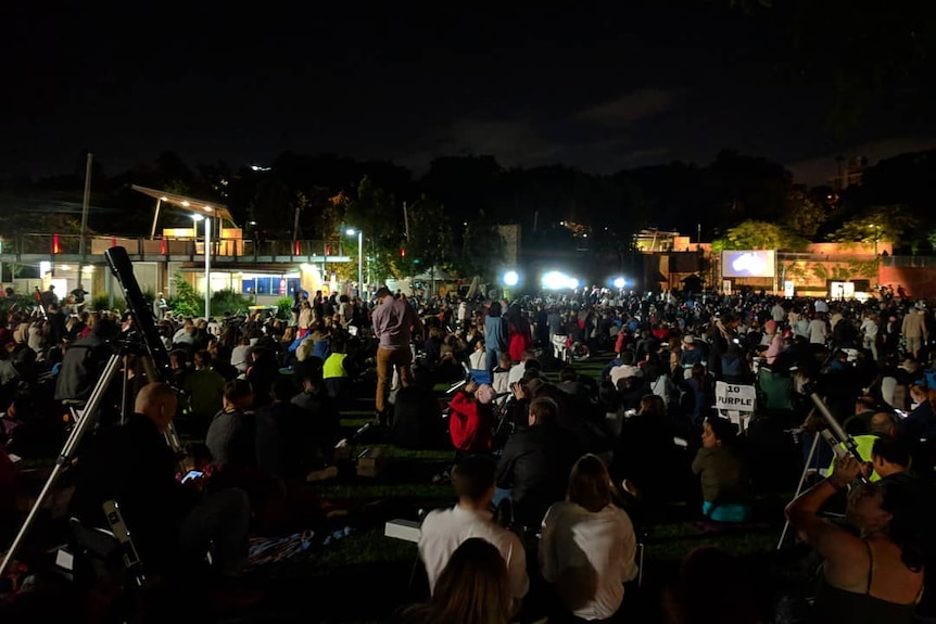 More than a hundred people look through telescopes and binoculars at night