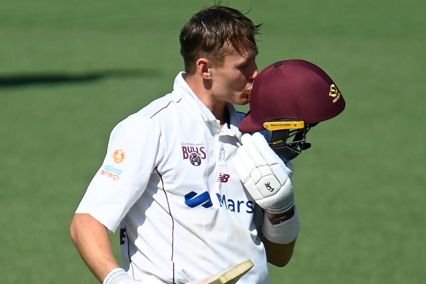 A Queensland Sheffield Shield batter kisses his helmet as he celebrates scoring a century.