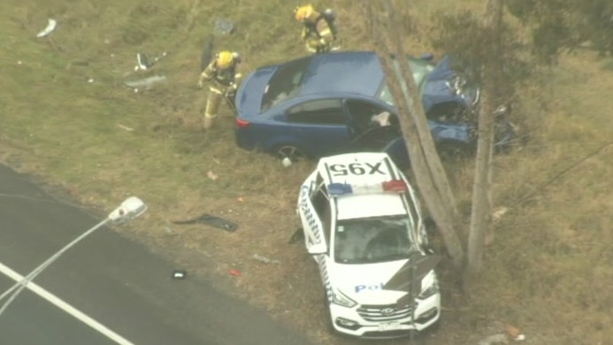 A blue sedan and a police car are damaged by the side of a road.