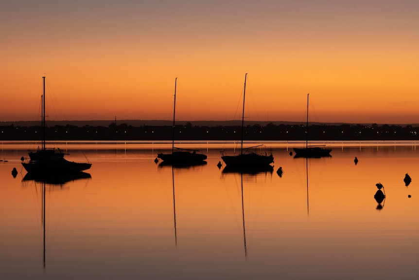 Boats with an orange sky and the orange also reflected on the water. 