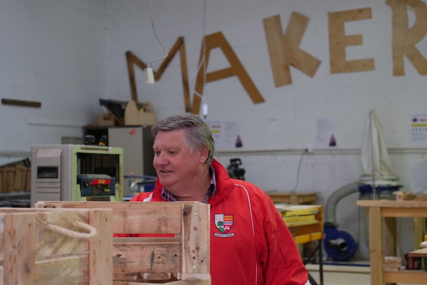 A man looks at wooden crates inside a large room with the word 'Maker' on the back wall.