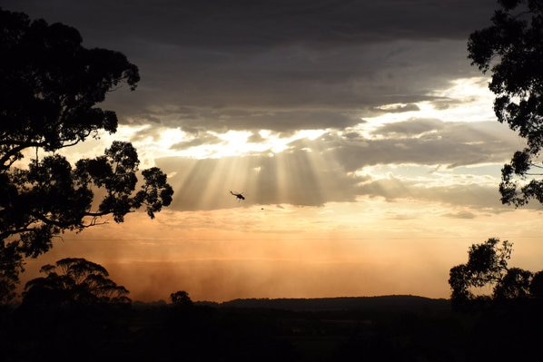 A waterbomber is silhouetted against a golden sky as sun breaks through the clouds over the bushfire