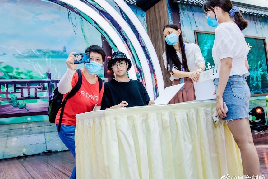 A group wearing masks take a photo around a young man sitting behind a desk.