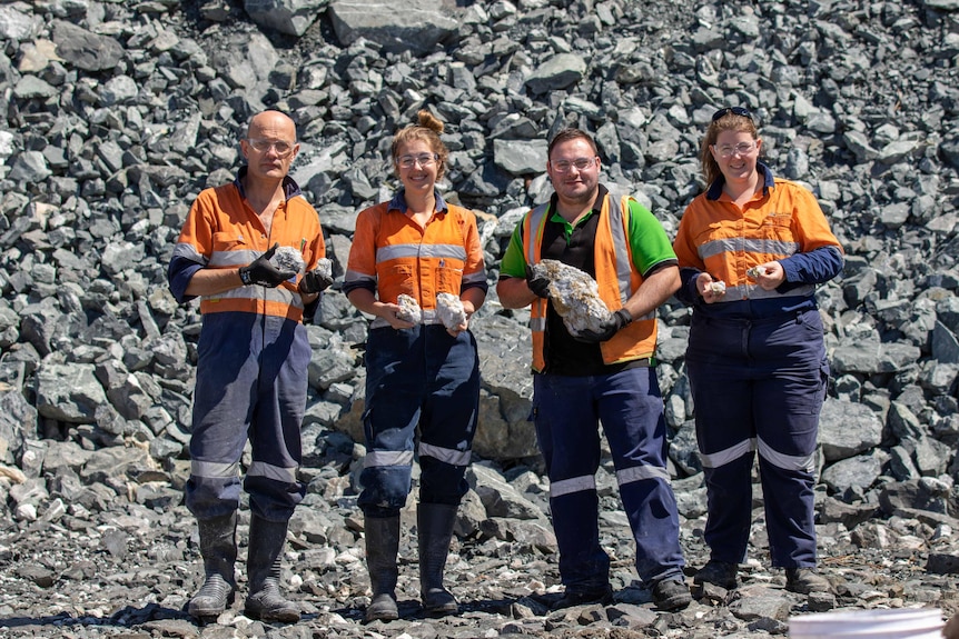Four mine workers wearing high-vis workwear holding gold specimens at a mine site.  