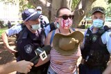 A woman with a shaved head is flanked by two police officers