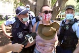 A woman with a shaved head is flanked by two police officers