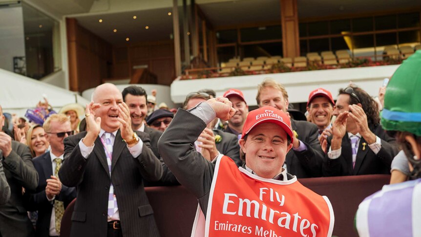 A young man with down syndrome cheers at a horse racing meet.