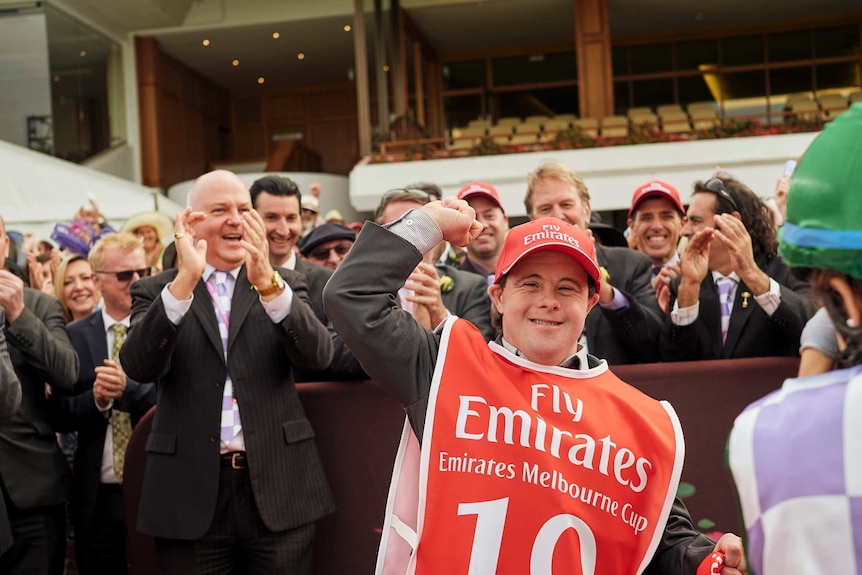 A young man with down syndrome cheers at a horse racing meet.