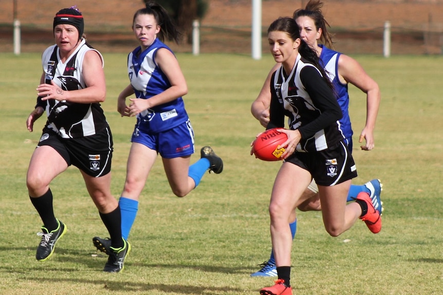 Women run down a field during a football game in country Victoria.