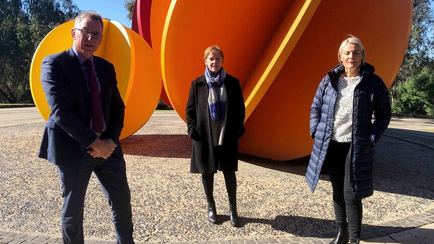 A man and two women standing in front of an orange sculpture