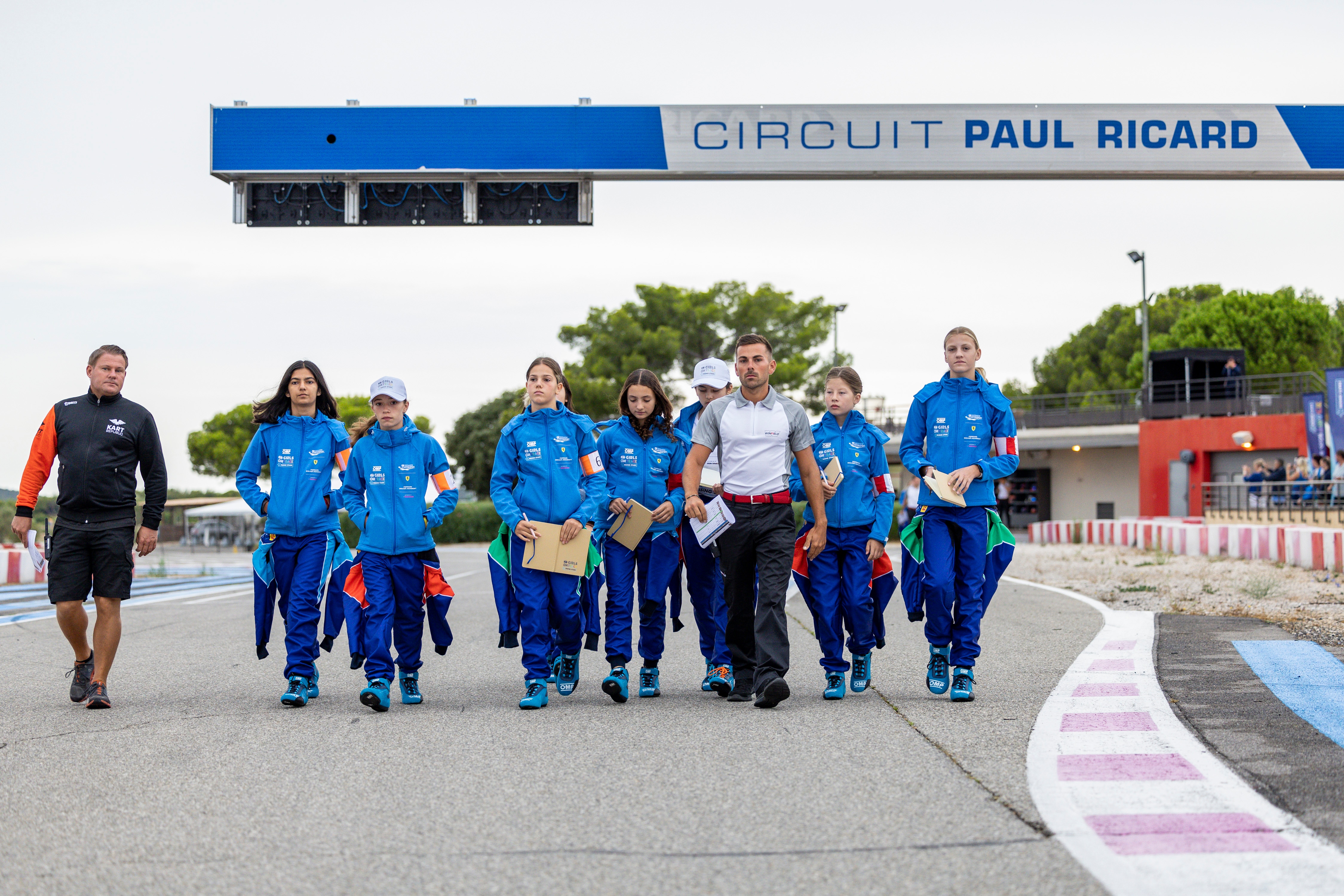 A group of people in blue racing suits walk on a track.