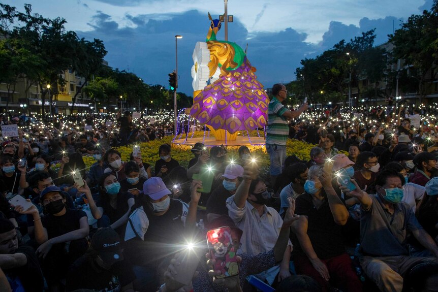 Thousands of protesters sit and hold mobile phones aloft, pointing the lights from the devices in the same direction.