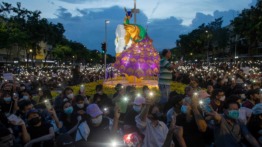 Thousands of protesters sit and hold mobile phones aloft, pointing the lights from the devices in the same direction.