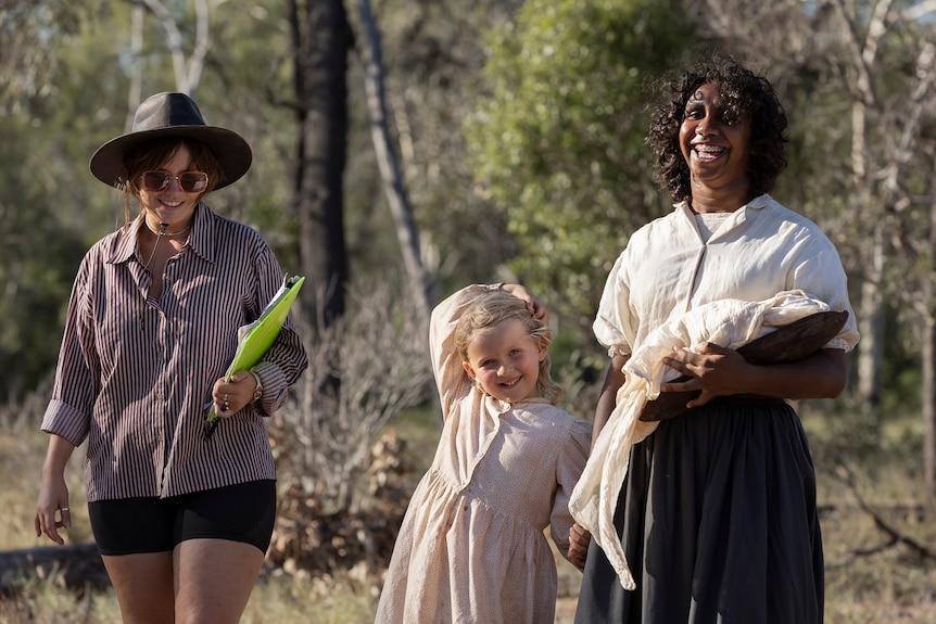 Joanna Joy holds a folder and is alongside little girl Ella, who is holding actress Zalhi Hayden's hand.