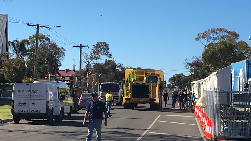 A large truck moves down a suburban street in Kalgoorlie-Boulder, guided into place by workers.