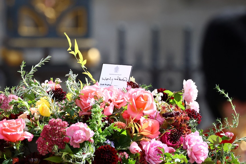 A note stands among colourful flowers atop the Queen's coffin. 