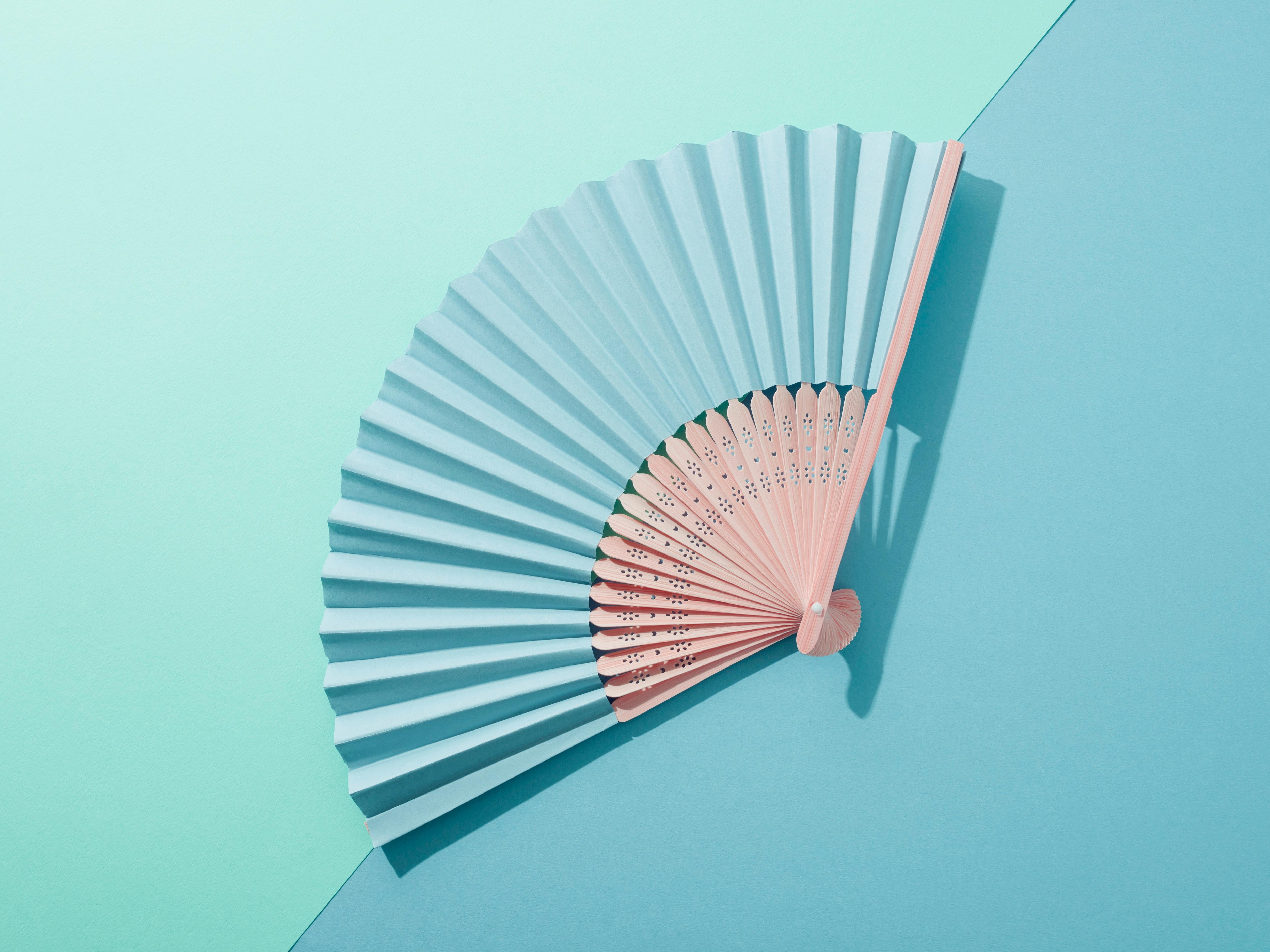 A blue hand fan open on a blue and green background. 