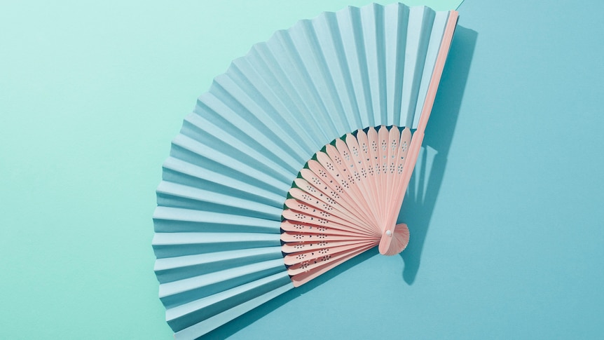 A blue hand fan open on a blue and green background. 