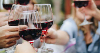 Sets of hands clink glasses of red wine together.