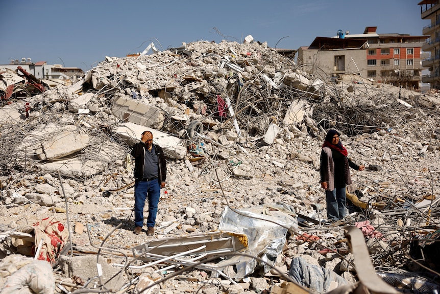 A man and woman stand among rubble. 