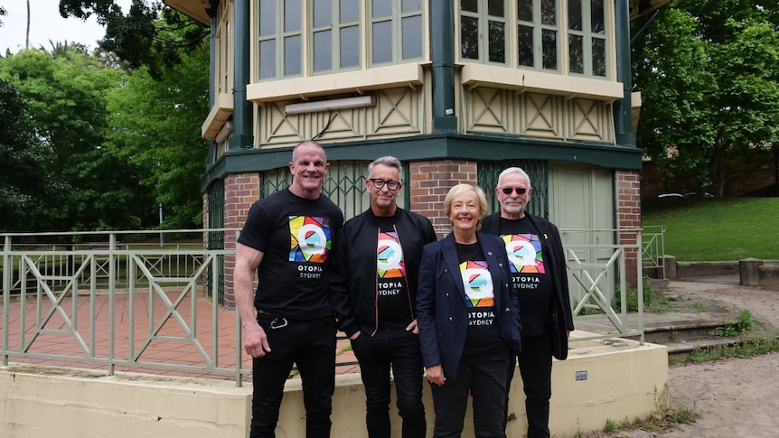 Four people pose in front of a bandstand building