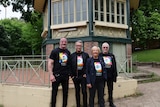 Four people pose in front of a bandstand building