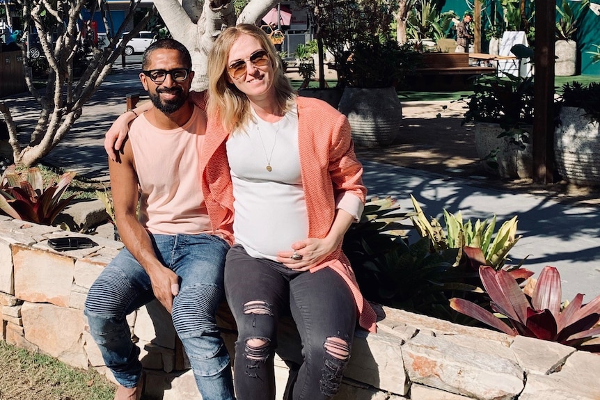 Cassie White holding her baby bump and sitting beside her partner.