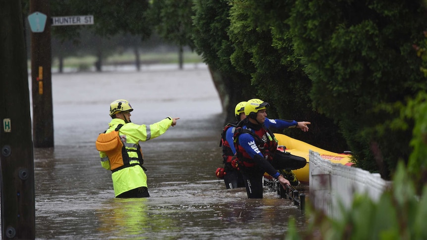 NSW Fire and Rescue officers wade through floodwaters next to the inflatable rubber boat.