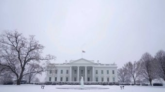 Snow covers the lawn in front of a White house with a bare tree beside it.