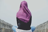 Back of woman in hijab, sitting on bridge.