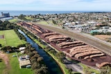 An aerial view of a large yard with thousands of large wooden logs, with the ocean in the distance.