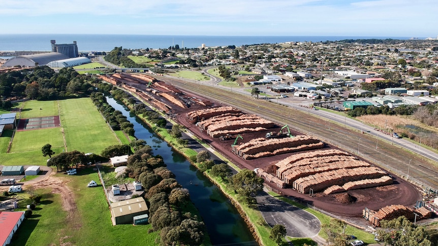 An aerial view of a large yard with thousands of large wooden logs, with the ocean in the distance.