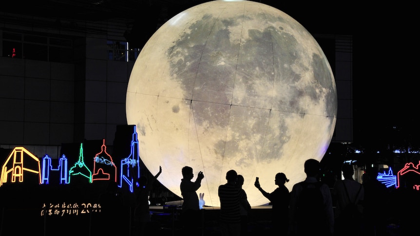 People stand in front of a moon installation at the shopping street Nanjing Road.