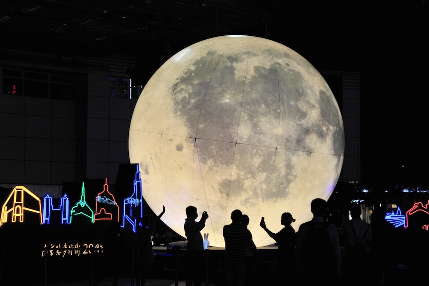 People stand in front of a moon installation at the shopping street Nanjing Road.