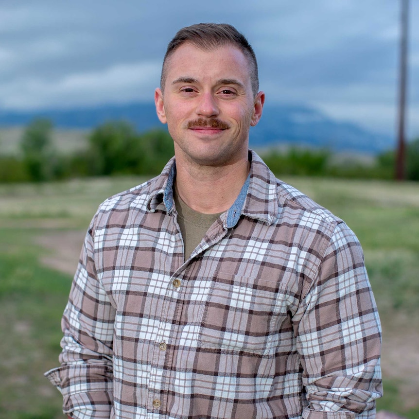 A man in a check shirt smiling while standing in a field