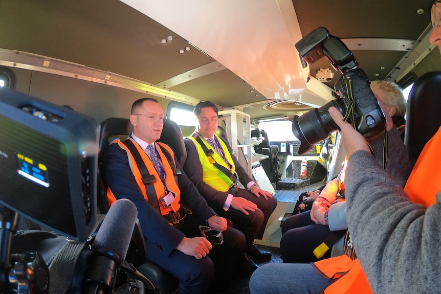 Men in high-vis sit inside an armoured military vehicle.