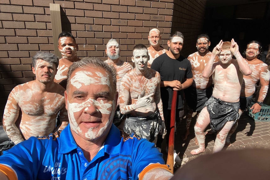 A man takes a selfie of himself and a group of buys with ochre on their bodies