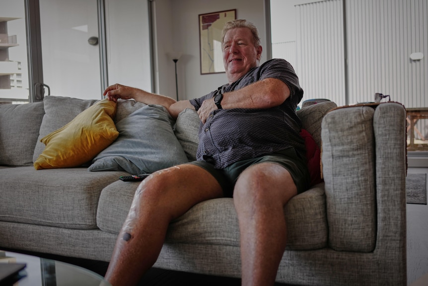 A man sitting on his couch wearing a shirt and shorts.