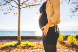Woman stands near water holding her early pregnant stomach in story about when everyone is excited about your pregnancy but you